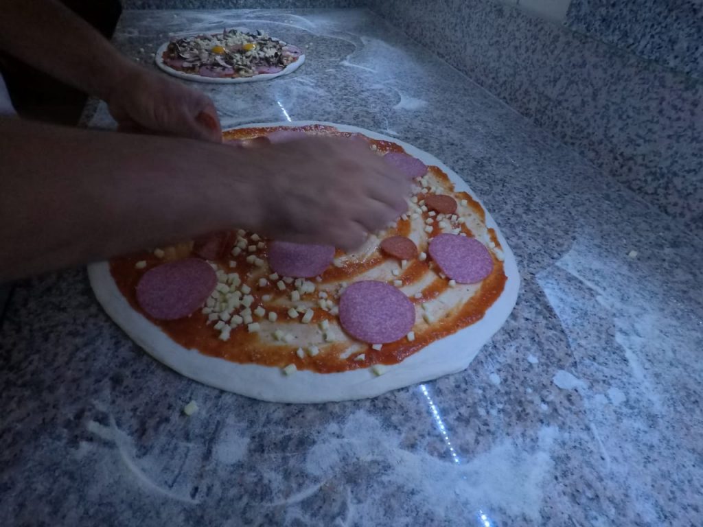 Pizzateig wird von Hand mit Salami belegt