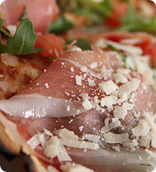 Nahaufnahme einer Pizza mit Parmaschinken, Parmesan und Rucola
