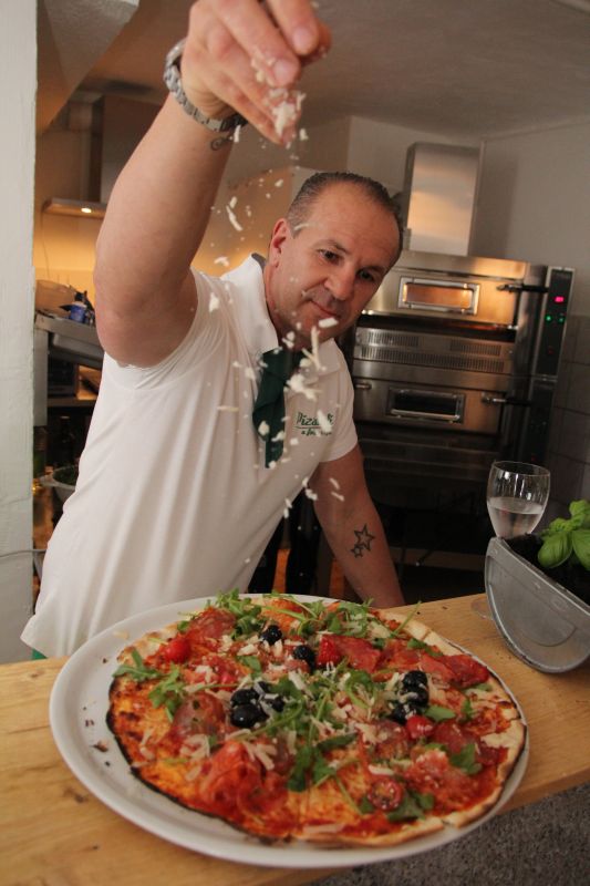 Pizzabäcker bestreut eine frisch gebackene Pizza mit Käse